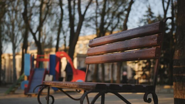 A lone empty recreation bench stands near the playground in the sunset light.