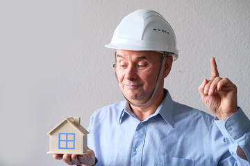 elderly male agent, a builder in a protective helmet, glasses offers to rent, buy a house, shows a model of a house, a mortgage concept, advice on buying a property