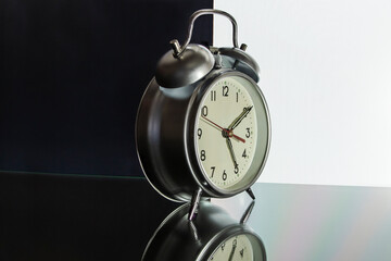 Classic alarm clock on a black and white background with reflection on the surface. Concept for advertising and design. Close-up.