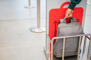 Woman checking backpack metal cage checking carry-on luggage at airport.