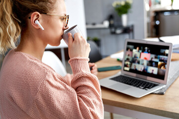 Young female teacher drinking coffee during online class