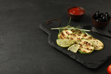 Delicious grilled zucchini slices served with lime and rosemary on black table. Space for text