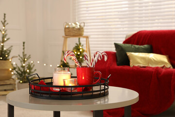 Candles and red cup with candy canes on white table in decorated room. Christmas interior design