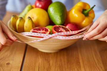 Close up of hand nutritionist, dietitian measuring bowl with healthy vegetables and fruits