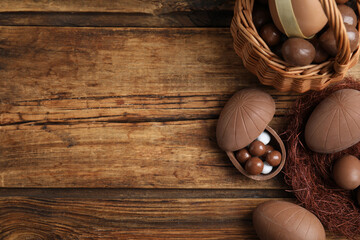 Obraz na płótnie Canvas Flat lay composition with tasty chocolate eggs, wicker basket and decorative nest on wooden table. Space for text