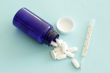 blue medicine bottle with white pills and mercury thermometer on blue background