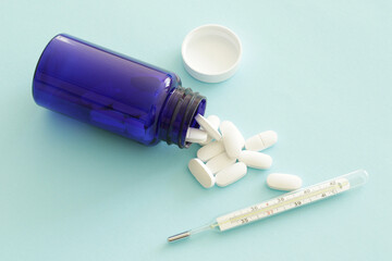 blue medicine bottle with white pills and mercury thermometer on blue background