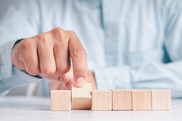 Businessman wearing a blue shirt, arranging the empty wooden blocks with his hands. Which is placed on a white wooden table. Business strategy and action plan. Copy space.