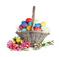 Fototapeta na wymiar Wicker basket with bright painted Easter eggs and spring flowers on white background