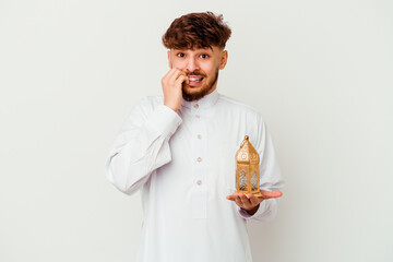 Young Moroccan man wearing a typical arab clothes holding a ramadan lamp isolated on white background biting fingernails, nervous and very anxious.