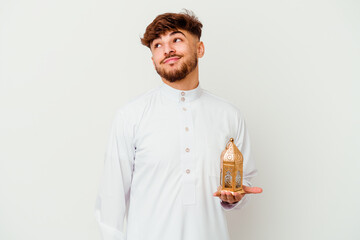 Young Moroccan man wearing a typical arab clothes holding a ramadan lamp isolated on white background dreaming of achieving goals and purposes