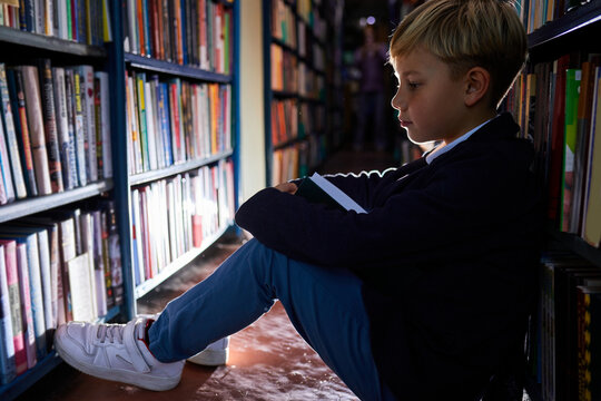 diligent boy learns day and night, sits reading a book in library on the floor, erudite boy was carried away by the book