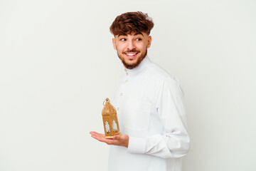 Young Moroccan man wearing a typical arab clothes holding a ramadan lamp isolated on white background looks aside smiling, cheerful and pleasant.