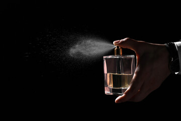 Man spraying luxury perfume on black background, closeup