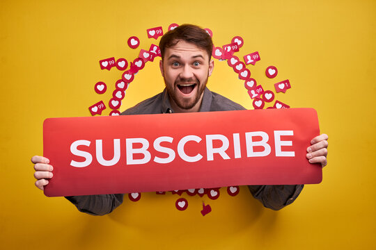 Happy male asking recommending to subscribe, pay attention, holding title in hands. Social media concept. Isolated yellow background