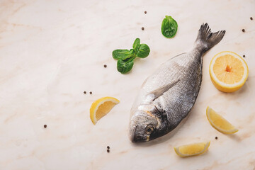 Dorado fish, lemon and green leaves on marble table with water drops and black pepper
