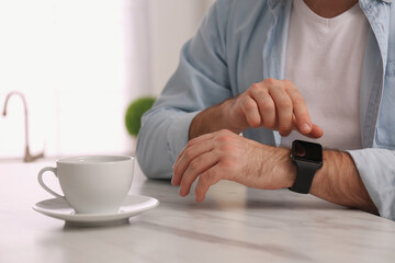 Fototapeta na wymiar Young man using smart watch at table in kitchen, closeup