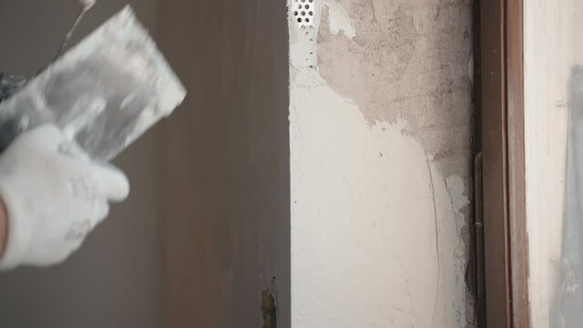 Construction worker in protective gloves using metal spatula for putty walls, repairman filling spatula with spackling paste and covering cement wall surface. Builder leveling wall and angle near the