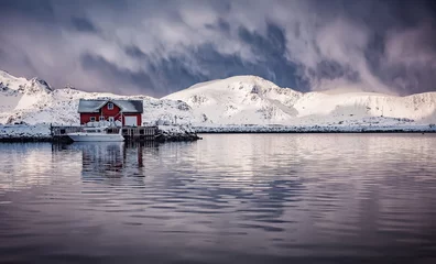 Wall murals Reinefjorden Wonderful winter view on snowcapped mountains, red fishing hut and cloudy sky with reflection. Typical nature landscape of Lofoten islands. Norway. Travel adventure and freedom concept.