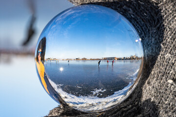 View through my lens ball of people skating on a frozen lake on a sunny winter day