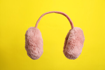 Fluffy earmuffs on yellow background. Stylish winter accessory