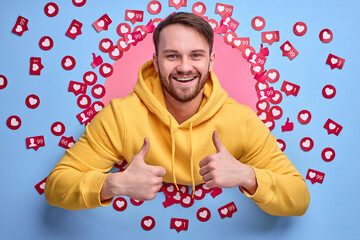 young male blogger is happy to get a lot of likes and views, stand among heart signs buttons, excited and cheerful, smiling. portrait