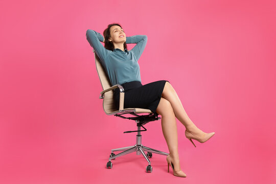 Mature Businesswoman Relaxing In Comfortable Office Chair On Pink Background