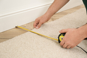 Worker with measuring tape installing new carpet indoors, closeup