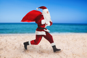 Santa Claus with red sack on beach near sea . Christmas vacation