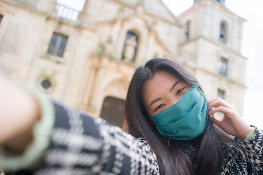 selfies and travel in times of covid19 - young happy and beautiful Asian Korean woman in surgical mask vs covid  taking selfie photo enjoying city in Europe