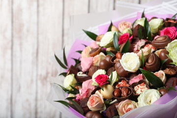 Beautiful bouquet of flowers and chocolate candies on white wooden background, closeup. Space for text