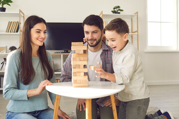 Happy family with child taking blocks from tumble tower. Smiling young Caucasian couple with little...