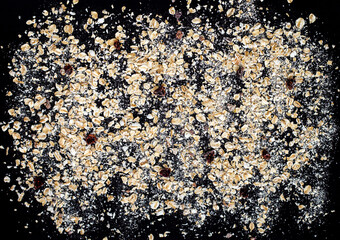 top view of oat flakes scattered on a black background, a pattern of instant oatmeal, healthy breakfast, precooked porridge with freeze-dried berries