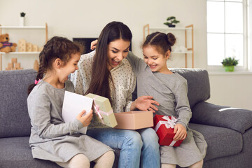 Happy little kids making surprise for mommy. Cute twin daughters giving mom presents and card and wishing her love and happiness. Excited young woman opens gift box children gave her on Mother's Day