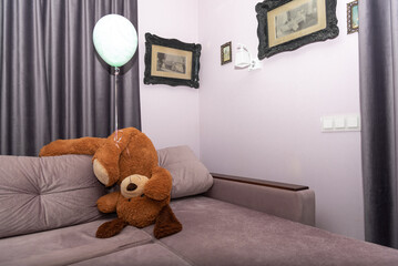 Handstand stuffed toy with balloon. Funny Teddy bear turned upside down on sofa, falling over. 