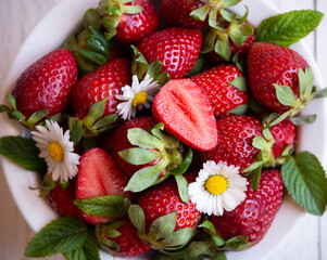Fresh strawberries in white bowl with leaves and flowers