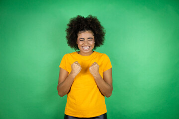 African american woman wearing orange casual shirt over green background very happy and excited...