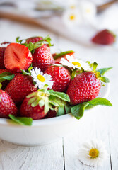 Fresh strawberries in white bowl with leaves and flowers