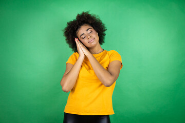 African american woman wearing orange casual shirt over green background sleeping tired dreaming and posing with hands together while smiling with closed eyes.