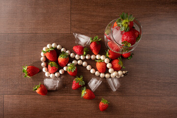 Strawberries, details of strawberries with ice cubes and a string of pearls on a table, black background, top view.