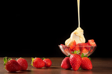 Strawberries, crystal bowl with strawberries and condensed milk on a table, black background,...