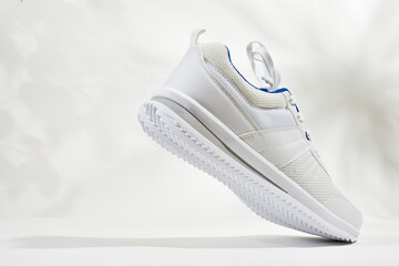 White sports sneakers with shoelace on a white wall background. Man sneakers for fitness. White sneaker with leather accents.