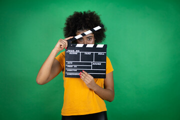 African american woman wearing orange casual shirt over green background holding clapperboard very...
