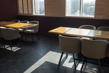 Cozy sunny interior of the cafe. Beautiful direct shadows on wooden tables. Empty cafe during lockdown.