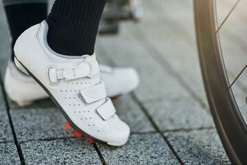 Close up shot of legs of female cyclist wearing cycling shoes standing with her bike