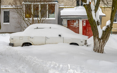 City street after blizzard. Stuck cars under the snow and ice. Buried vehicle in snowdrift on the road. Parking lots in winter after heavy snowfall. Uncleaned roads. Record-breaking amounts of snow.