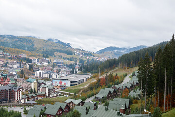 Fototapeta na wymiar Beautiful landscape view over ski resort in Ukraine. Mountains covered with evergreen forest and fog cloudy autumn day. Getaway vacation into natural surrounding. Mountain resort recreation.