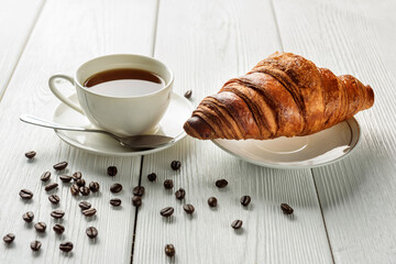 A cup of coffee and a croissant on a table with sprinkled coffee beans.