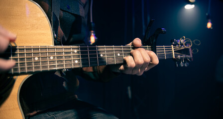 Obraz na płótnie Canvas Close up a man plays an acoustic guitar in a dark room.