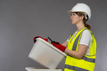 Woman builder with a plastic box in her hands. Girl in yellow vest. Box in hand as a symbol of...